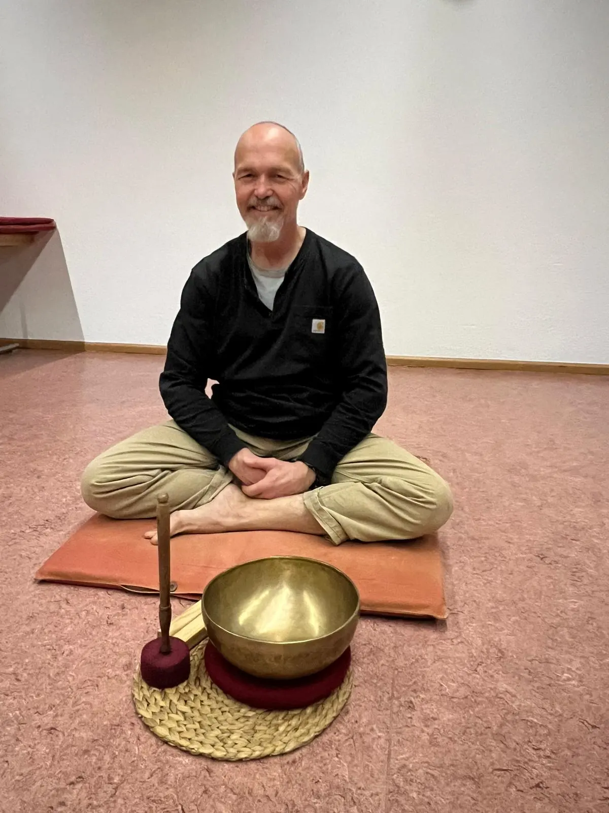 Dieter Schleier sitzt lächelnd auf seinem Meditationskissen, vor ihm eine Klangschale
