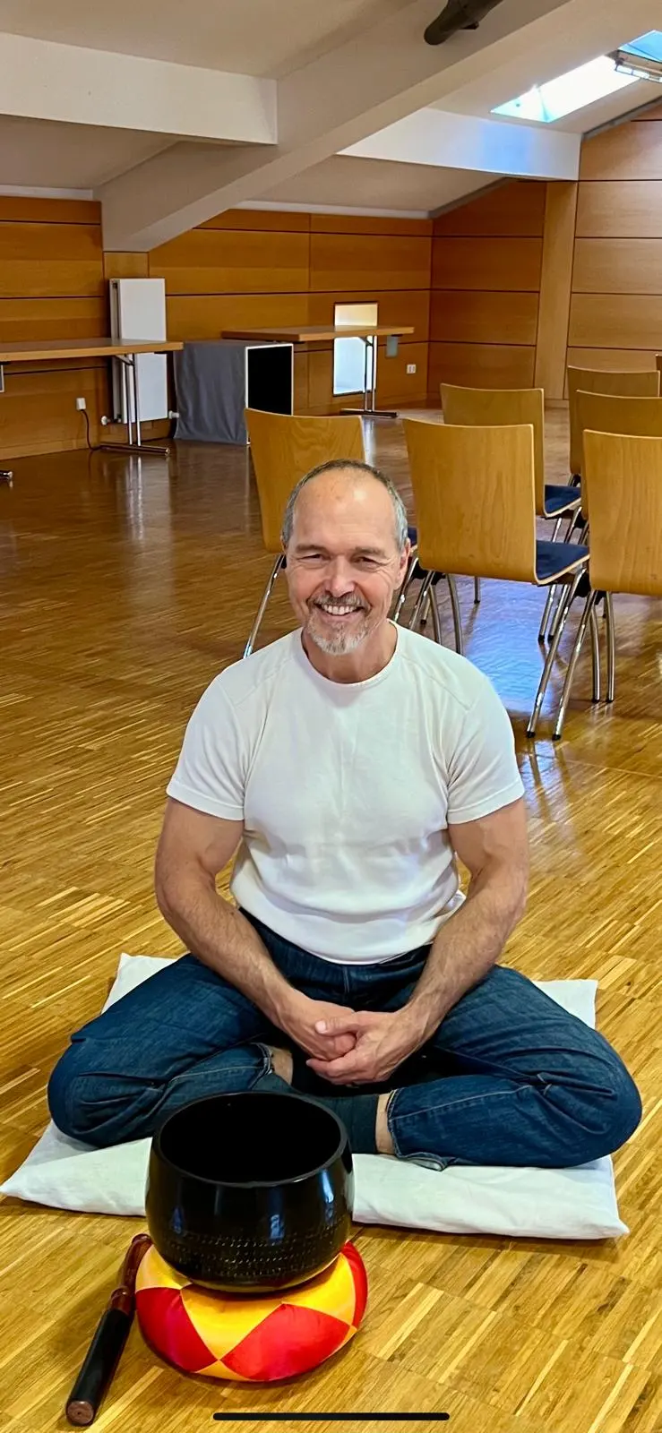 Dieter Schleier sitzt lächelnd im Meditationsraum, vor ihm eine Klangschale