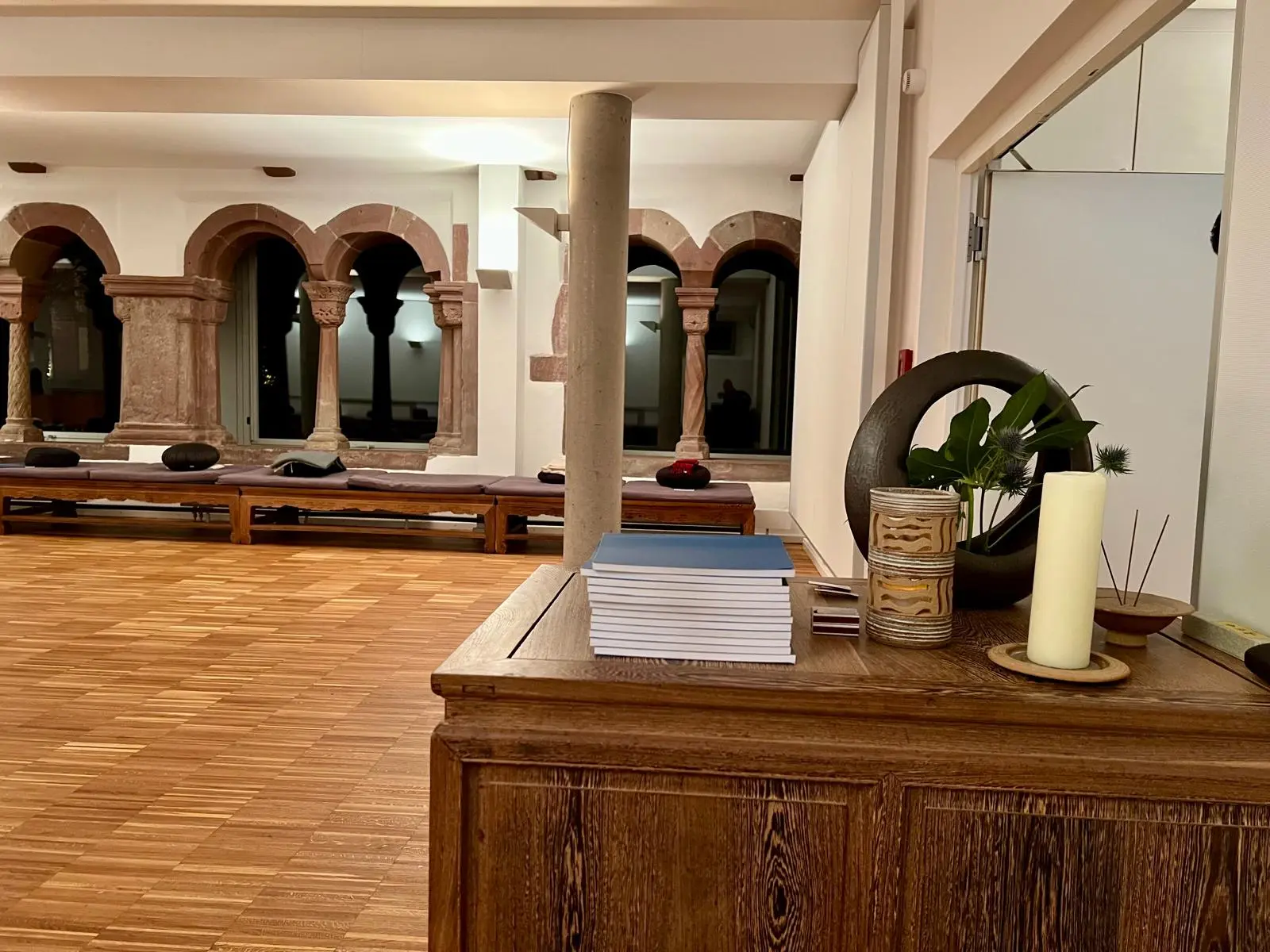 Ruhiger Meditationsraum mit Holzboden, Kerze und historischen Bogenfenstern